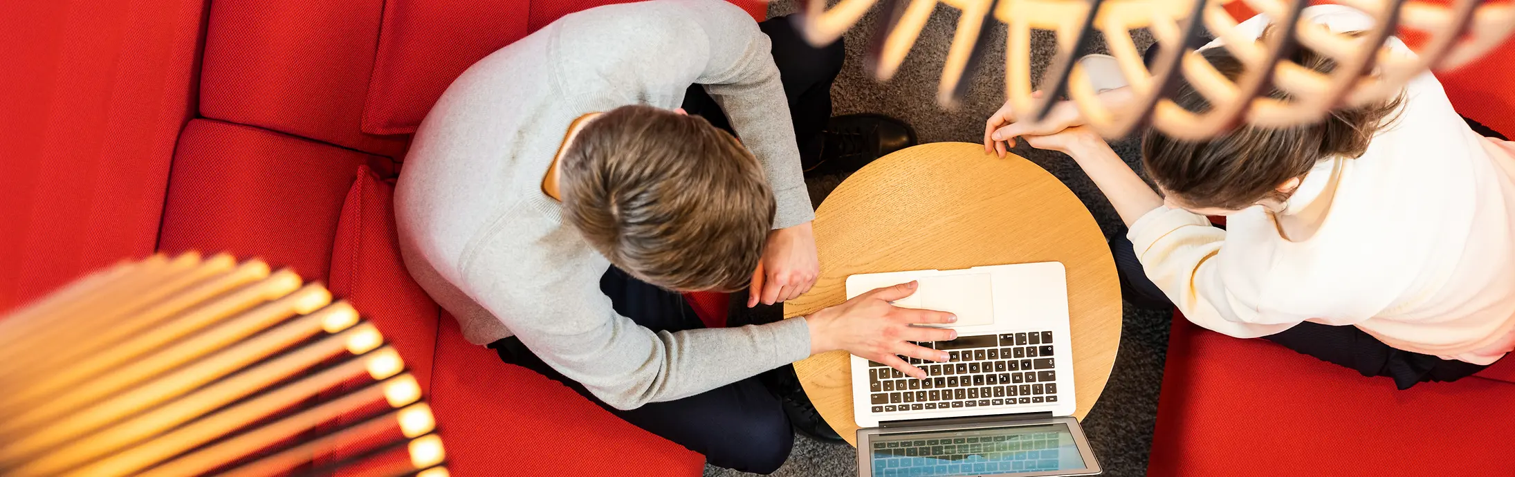 Twee mensen zitten op een rode sofa en werken samen op een laptop 