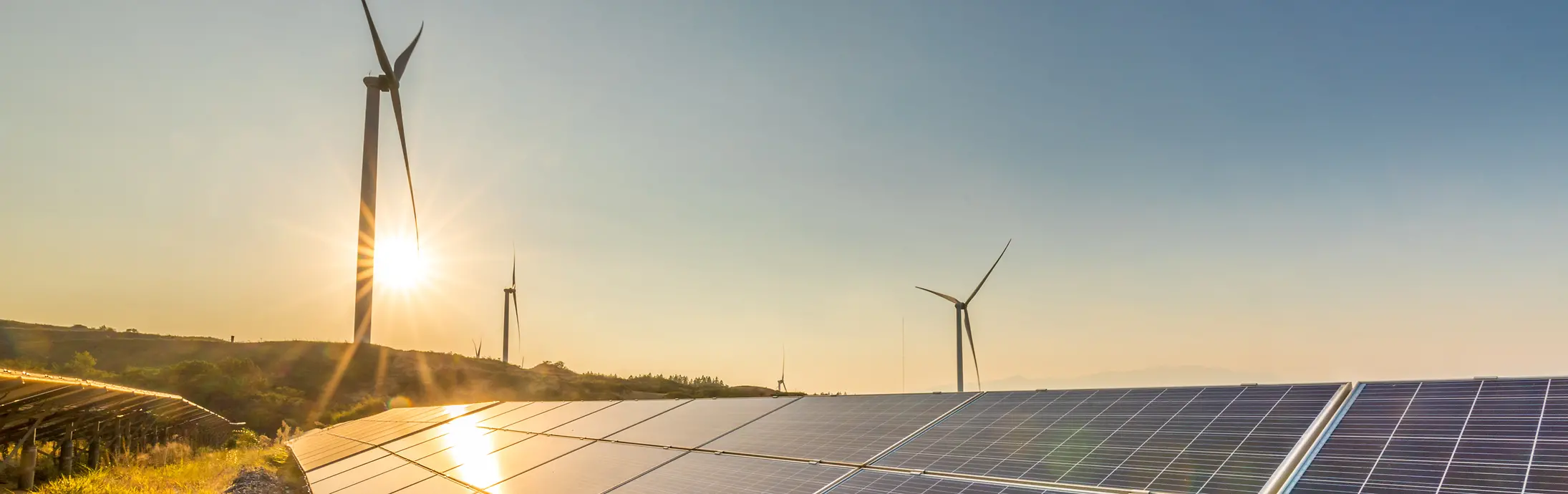 Zonnepanelen bij zonsondergang met windmolens op de achtergrond